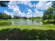 Community pond with fountain, surrounded by lush green grass and mature trees on a sunny day at 36137 Lake Chase Blvd # 102, Zephyrhills, FL 33541