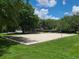 Sand volleyball court surrounded by lush green grass and mature trees on a sunny day at 36137 Lake Chase Blvd # 102, Zephyrhills, FL 33541