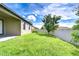 Backyard with green grass and a large tree with white vinyl fence and blue skies at 11011 Little Blue Heron Dr, Riverview, FL 33579