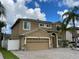 Two-story tan home with a two-car garage, blue door, and solar panels, situated on a paver driveway at 1205 Sweet Gum Dr, Brandon, FL 33511