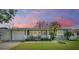 Charming single-story home featuring a white picket fence, attached garage, and freshly manicured lawn under a lovely pink sunset sky at 2025 Jefferson Ave, Dunedin, FL 34698