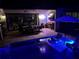 Illuminated pool at night featuring a dining area, outdoor kitchen, and stylish lounge chairs for ultimate relaxation at 31889 Tortuga Shore Loop, Wesley Chapel, FL 33545