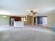 Open-concept living room features a ceiling fan, tan carpet, and view of the kitchen at 12121 Tree Haven Ave, Gibsonton, FL 33534