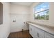 Bright laundry room with wood-look vinyl floors, granite counters, white cabinets, and large window for natural light at 132 Pennsylvania Ave, Palm Harbor, FL 34683
