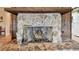 Close-up of a stone fireplace with decorative floral arrangement and tools, with a kitchen in the background at 855 Pinewood W Ter, Palm Harbor, FL 34683