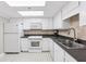 Functional kitchen featuring white appliances, light tile flooring and dark countertops at 1 Key Capri # 302E, Treasure Island, FL 33706