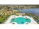 Aerial view of a community pool area, with palm trees, lounge chairs, umbrellas, and a lake and playground nearby at 11019 Leland Groves Dr, Riverview, FL 33579