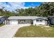 Single-story home featuring a paved driveway, attached garage, manicured lawn and covered front porch at 1144 Woodbrook Dr, Largo, FL 33770