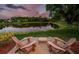Relaxing backyard with Adirondack chairs overlooking a serene lake surrounded by lush greenery and a picturesque sky at 1303 Forestedge Blvd, Oldsmar, FL 34677