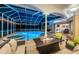 Nighttime view of a screened-in pool with a hot tub and a fire pit table in the outdoor living area at 1303 Forestedge Blvd, Oldsmar, FL 34677