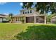 Backyard view of the home with a spacious lawn, mature trees, well-maintained exterior, and screened lanai at 8704 Winsome Way, Land O Lakes, FL 34637