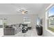 Bright living room with a gray sectional sofa, ceiling fan, and a large window overlooking the yard at 81 Rain Lily Ave, Spring Hill, FL 34609