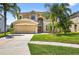 Beige two-story home featuring a two-car garage, manicured lawn, and tropical palm trees at 19028 Narimore Dr, Land O Lakes, FL 34638