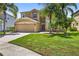 Beige two-story home featuring a two-car garage, manicured lawn, and tropical palm trees at 19028 Narimore Dr, Land O Lakes, FL 34638