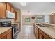 The kitchen features stainless steel appliances, light wood cabinets, tile flooring, and bar seating looking towards dining area at 15420 Quail Woods Pl, Ruskin, FL 33573