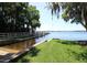 Waterfront view featuring a boat launch, dock and grassy shoreline with mature trees and a glimpse of the open water at 4147 Grandchamp Cir, Palm Harbor, FL 34685