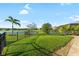 Expansive backyard features a well-maintained lawn, elegant landscaping, and black metal fence with a lake view at 12830 24Th Street E Cir, Parrish, FL 34219