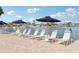 View of a pool deck with a row of lounge chairs with umbrellas and the water in the background on a sunny day at 400 64Th Ave # 202, St Pete Beach, FL 33706