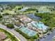 Community aerial view featuring tennis courts, a pool, clubhouse, parking, a tranquil lake, and lush landscaping at 511 Foxglove Cir # B, Sun City Center, FL 33573