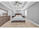 A spacious gray main bedroom featuring a tray ceiling, ceiling fan, carpet, and a dresser at 3013 W Crest Ave, Tampa, FL 33614