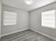 Neutral-walled bedroom featuring gray wood-like flooring and natural light from two windows at 8017 Tudor Pl, Tampa, FL 33610