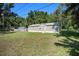 Exterior shot featuring lush lawn, shed, and cozy single-story home with a wooded backdrop at 2121 Odessa Gardens Ln, Odessa, FL 33556