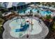 Aerial view of a water park with a colorful splash pad and a larger pool surrounded by palm trees at 4957 Seafoam Trl, Bradenton, FL 34211