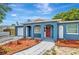 Blue single-story house with arched entryways and a red front door, surrounded by neatly arranged mulch beds at 8033 Norwich Dr, Port Richey, FL 34668