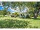 Landscaped front yard view of home with green lawn, mature trees, and vibrant blue sky at 1857 N Belleair N Rd, Clearwater, FL 33764