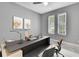 Modern home office with a large desk, two windows, and neutral gray walls offers a productive workspace at 3241 Evening Breeze Loop, Wesley Chapel, FL 33544