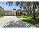 A beige house on a sunny day, with a well-manicured lawn, a tree, and a two-car garage at 13310 Tiger Lilly Ln, Tampa, FL 33625