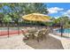 Inviting patio area with shade umbrellas and a dining table, located adjacent to a tennis court and pool at 1628 Long Bow Ln, Clearwater, FL 33764