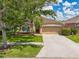 Inviting single-story home featuring a manicured lawn, mature tree, and convenient two-car garage at 27652 Sky Lake Cir, Wesley Chapel, FL 33544