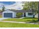 Charming single-story home featuring a well-maintained lawn, a blue painted driveway and a gray garage door at 7815 Shadow Run Dr, Largo, FL 33773