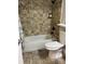 Bathroom features a shower-tub combo, decorative stone tile, and matching floors with a white toilet at 1400 Pine Glen Ln # D2, Tarpon Springs, FL 34688