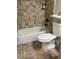 Bathroom features a shower-tub combo, decorative stone tile, and matching floors with a white toilet at 1400 Pine Glen Ln # D2, Tarpon Springs, FL 34688