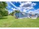 Charming home exterior with blue siding, awning, and spacious green yard against a bright sky at 35014 Carl Ave, Zephyrhills, FL 33541