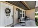 Detailed view of a white front door with wreath, exterior lights, and a cozy seating area on the porch at 1800 Mapleleaf Blvd, Oldsmar, FL 34677