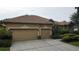 A tan two-car garage home with mature landscaping, side entrance, and well maintained driveway at 8731 Tantallon Cir, Tampa, FL 33647