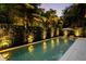 A luxurious backyard pool with integrated lounge chairs surrounded by illuminated, lush tropical landscaping at 4525 W Swann Ave, Tampa, FL 33609