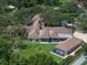 Aerial view of a home featuring a tennis court, manicured lawn, and mature trees on a sunny day at 1835 Alicia Way, Clearwater, FL 33764