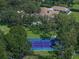 Aerial view showcases a blue tennis court amidst lush greenery and a spacious home at 1835 Alicia Way, Clearwater, FL 33764