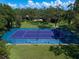 Aerial view of a blue and purple tennis court nestled within lush greenery, offering a private recreational space at 1835 Alicia Way, Clearwater, FL 33764