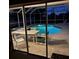 Illuminated enclosed pool and spa area with patio furniture visible through sliding glass doors during evening at 13986 Bonnie Brae Dr, Largo, FL 33774