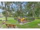 View of a fenced playground with slides, swings, and benches surrounded by lush greenery at 6332 Timberly Ln, Zephyrhills, FL 33542