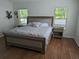 Primary bedroom featuring wood flooring, a king bed with neutral-toned upholstered headboard, and windows providing natural light at 12216 Southbridge Ter, Hudson, FL 34669