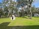 Backyard view with a brick oven, green lawn, and mature trees providing shade and a shed in the distance at 17926 Calkins Ct, Spring Hill, FL 34610
