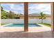 This enticing pool area is viewed from a covered patio, offering travertine surround, white fence, and landscaping at 1808 W Erna Dr, Tampa, FL 33603