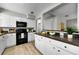 Kitchen with white cabinets, black appliances, dark countertops, hardwood floors, and a view into another room at 717 Pinewood Dr, Dunedin, FL 34698