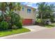 Two-story home with red garage door, lush tropical landscaping, and a glimpse of the screened-in pool area at 5955 Caldera Ridge Dr, Lithia, FL 33547